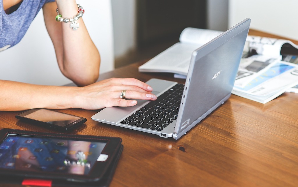 A person uses a laptop, next to a phone and tablet.